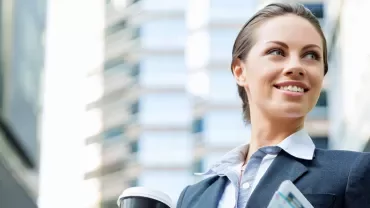 Person in business attire holding coffee and tablet outdoors.