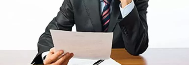 Persoon in pak leest een document aan een bureau.